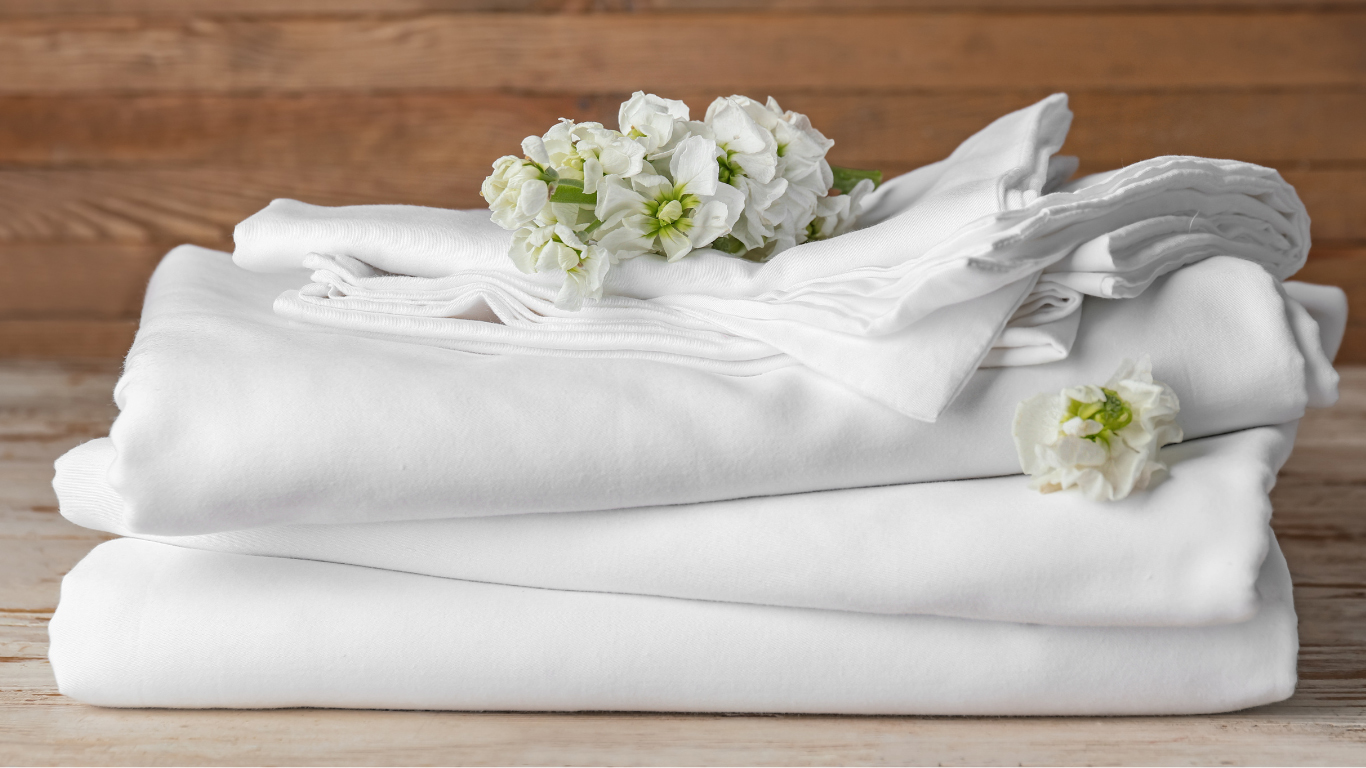 Stacked bed linen including fitted bedsheets, flat bedsheets, pillowcases, and duvet covers — designed for hotel comfort and long-lasting hospitality use.